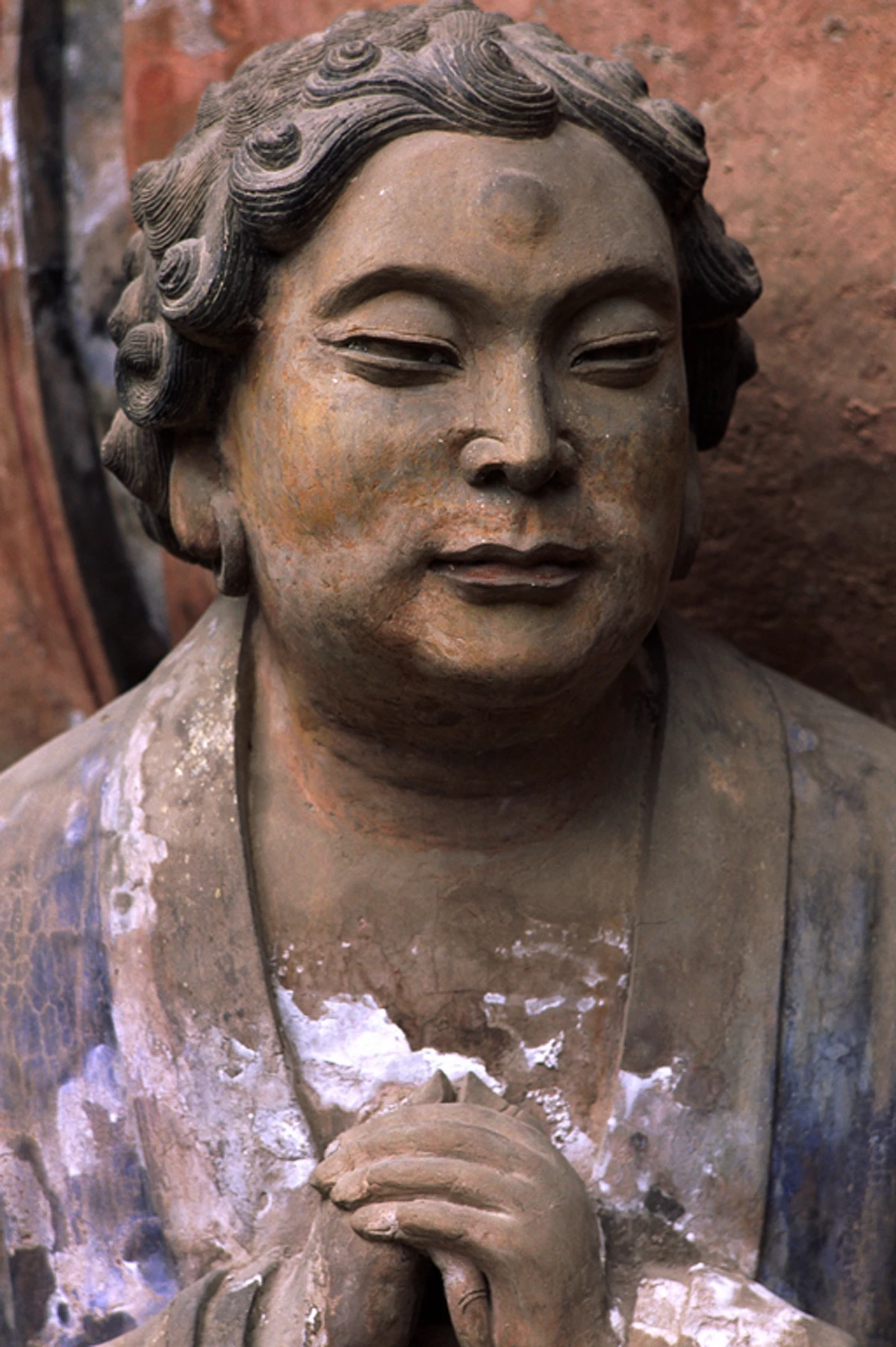 Close-up of a serene carved bodhisattva figure with detailed curly hair and hands in prayer, showing the refined stone carving technique