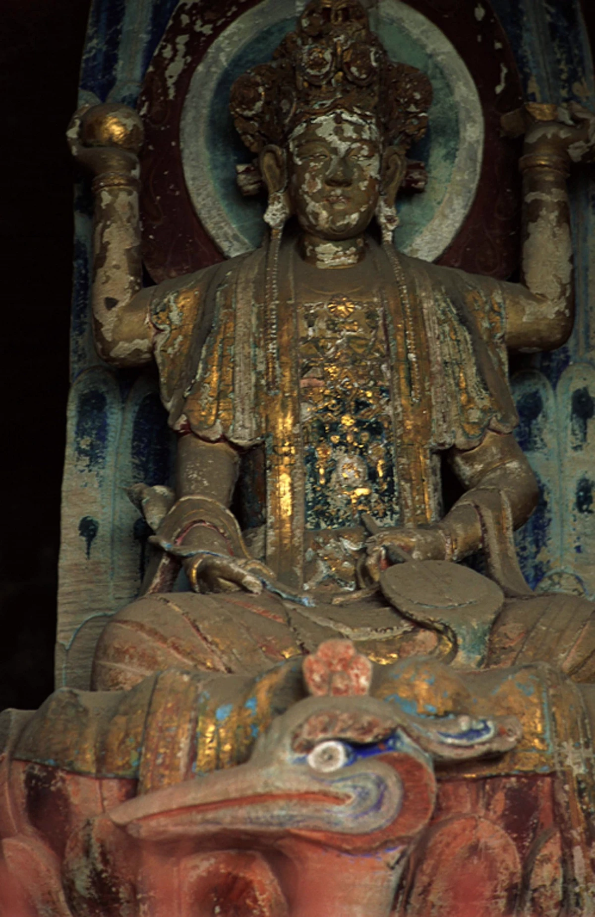 A gilded bodhisattva figure with ornate crown and halo, showing traces of gold leaf and centuries of weathering