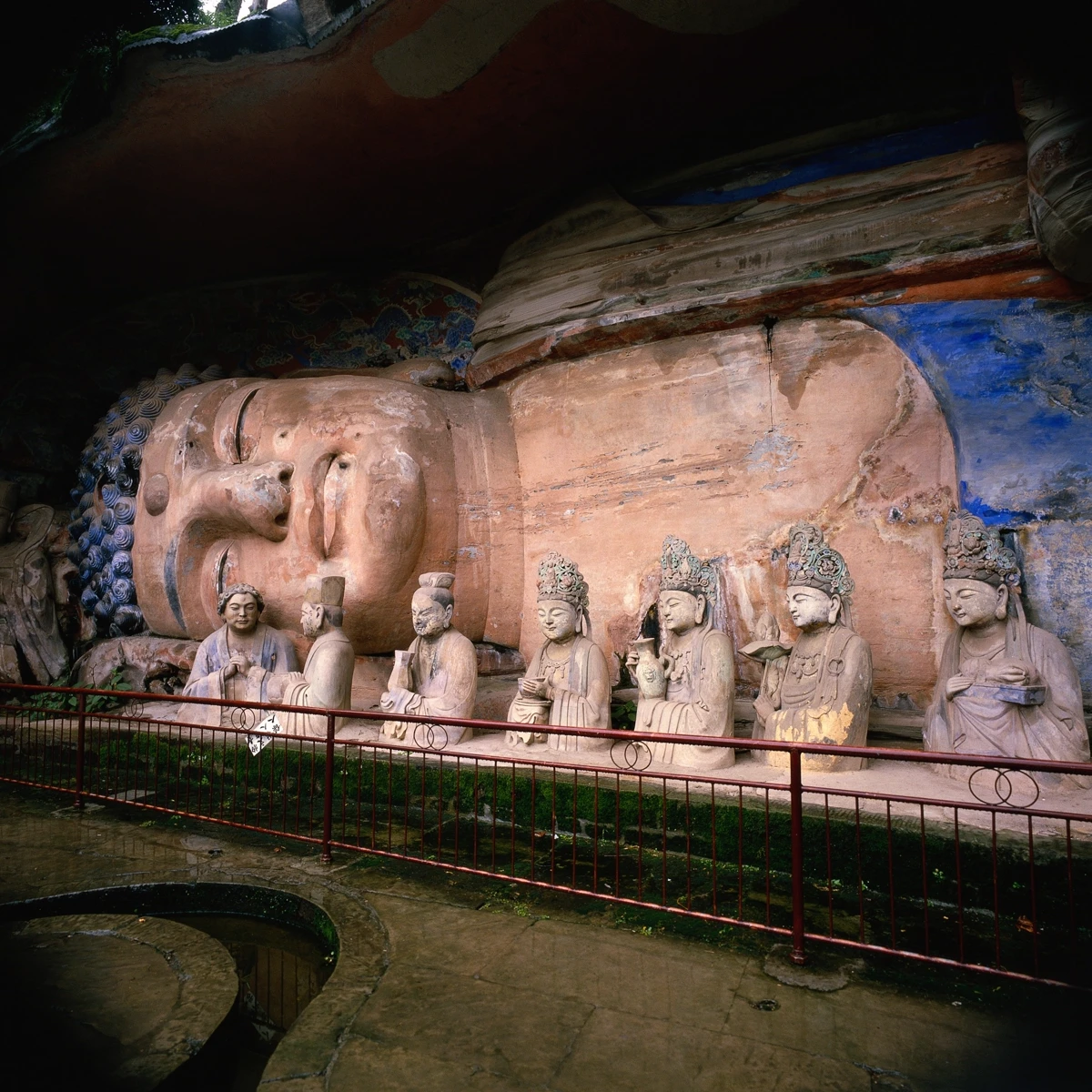 A monumental reclining Buddha (Nirvana scene) with seven smaller attendant figures seated in front, behind a red railing