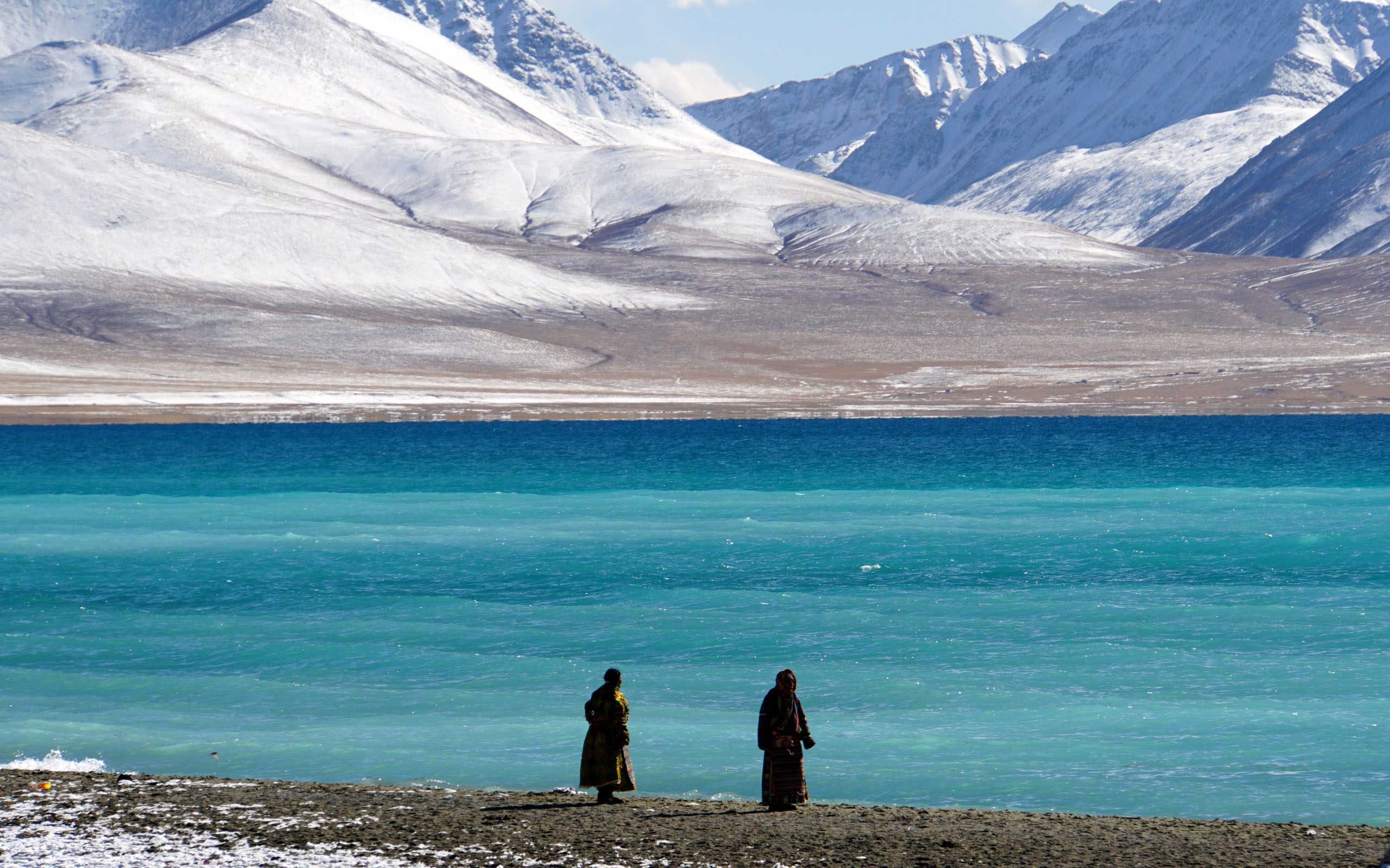 Namtso Lake, turquoise blue water stretching toward snow-capped mountains under a dramatic sky